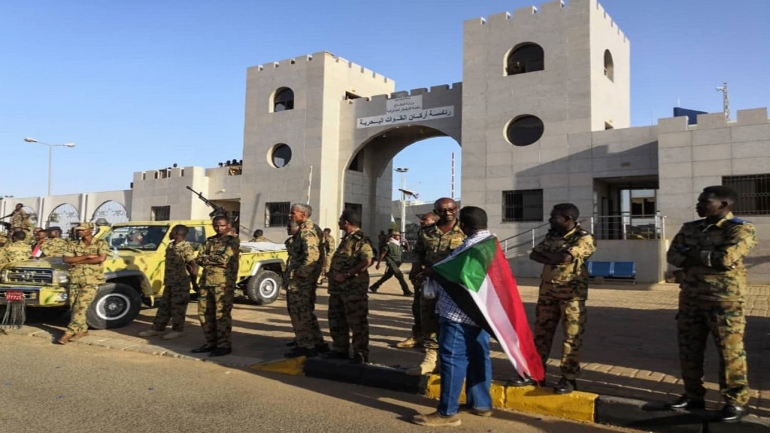 A Sudanese protester drapped in the national flag speaks with a soldier as they rally for a second day outside the military headquarters in the capital Khartoum on April 7, 2019. - Sudanese police fired tear gas at thousands of protesters who rallied outside the army headquarters for a second day urging the military to back them in demanding President Omar al-Bashir resign. (Photo by - / AFP)