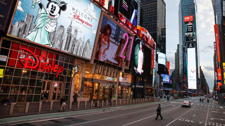A police officer walks across an empty 7th Avenue in a sparsely populated Times Square due to COVID-19 concerns, Friday, March 20, 2020, in New York. New York Gov. Andrew Cuomo is ordering all workers in non-essential businesses to stay home and banning gatherings statewide. "Only essential businesses can have workers commuting to the job or on the job," Cuomo said of an executive order he will sign Friday. Nonessential gatherings of individuals of any size or for any reason are canceled or postponed. (AP Photo/John Minchillo)