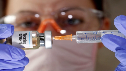 FILE PHOTO: A woman holds a small bottle labeled with a "Vaccine COVID-19" sticker and a medical syringe in this illustration taken April 10, 2020. REUTERS/Dado Ruvic/Illustration/File Photo