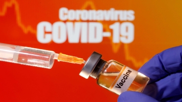 FILE PHOTO: A small bottle labeled with a "Vaccine" sticker is held near a medical syringe in front of displayed "Coronavirus COVID-19" words in this illustration taken April 10, 2020. REUTERS/Dado Ruvic/Illustration -/File Photo