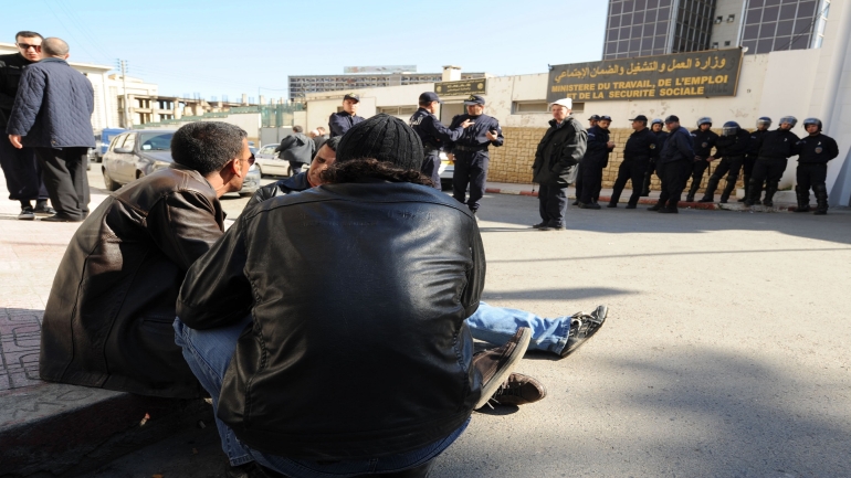 People gather during a protest against unemployment as policemen stand guard, on February 6, 2011 in front of the Ministry of Labour, in Algiers. Mounting grievances over spiraling costs and unemployment triggered riots this month, encouraged by public protests in Tunisia that forced its president Zine El Abidine Ben Ali to flee. AFP PHOTO FAROUK BATICHE (Photo credit should read FAROUK BATICHE/AFP/Getty Images)