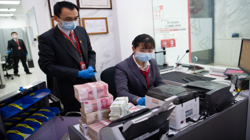 TAIYUAN, CHINA - MARCH 02: Staff wearing face masks work beside stacks of Chinese yuan banknotes at a China Guangfa Bank on March 2, 2020 in Taiyuan, Shanxi Province of China. Some banks in Shanxi resumed work on Monday amid novel coronavirus spread. (Photo by Wei Liang/China News Service via Getty Images)