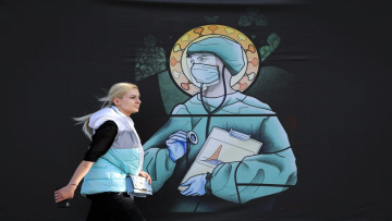 A woman walks by a depiction of a medical staff wearing protective equipment, executed in the style of orthodox icons, in Bucharest, Romania, Wednesday, April 29, 2020. The artwork, among others depicting medical staff in the manner of religious icons, created by designer Wanda Hutira, is part of a campaign called Thank You Doctors, meant to raise awareness to the work of medical staff fighting the COVID-19 pandemic. Following public pressure by Romania's influential Orthodox church the artworks, described as "blasphemous" will be removed from all locations in the Romanian capital, according to the agency behind the project. (AP Photo/Vadim Ghirda)
