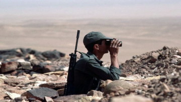 ca. October 1985, Western Sahara --- A Moroccan soldier looks through binoculars at the defense wall in Guelta-Zimmour, on the lookout for members of the Polisario. Morocco annexed and occupied parts of Western Sahara, and there is armed conflict between Moroccan occupying forces and the Polisario, a guerilla group fighting in support of the indigenous people of Western Sahara. --- Image by © Peter Turnley/CORBIS