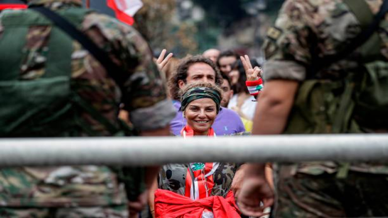 TOPSHOT - A protester draped in the Lebanese national flag flashes the victory gesture as she stands before Lebanese army soldiers during a demonstration on the seventh day of protest against tax increases and official corruption, in Zouk Mosbeh, north of the capital Beirut, on October 23, 2019. - The almost one-week-old massive street protests in Lebanon, sparked by a tax on messaging services such as WhatsApp, have morphed into a united condemnation of a political system seen as corrupt and beyond repair. (Photo by JOSEPH EID / AFP) (Photo by JOSEPH EID/AFP via Getty Images)