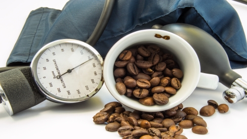 Coffee and blood pressure. Cup with coffee beans inside, surrounded by cuff and sphygmomanometer for measuring blood pressure. Concept of influence and effects of coffee on low or high blood pressure